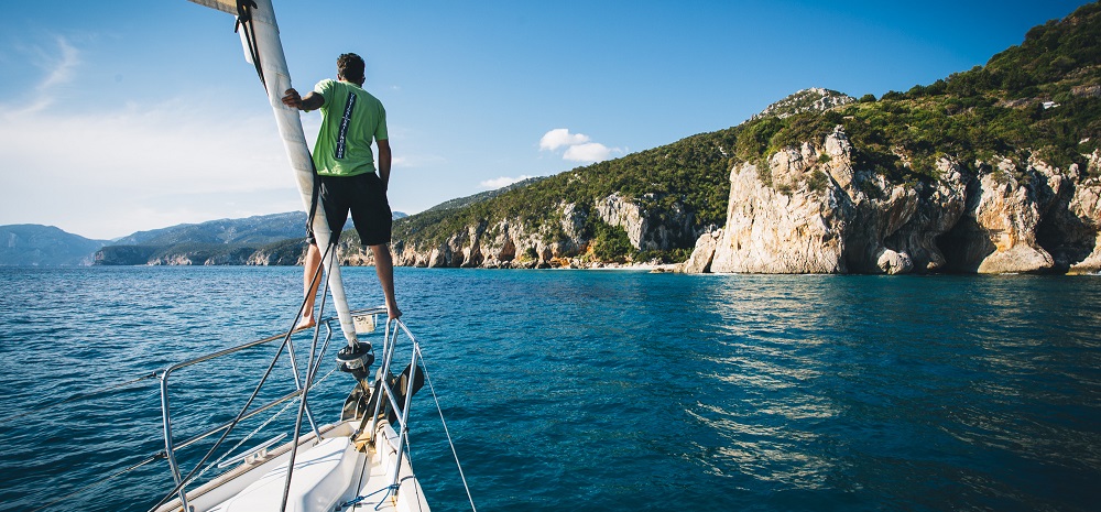 Abordage des falaises par la mer. Un homme debout sur la pointe du bateau juste au dessus d'une eau turquoise.