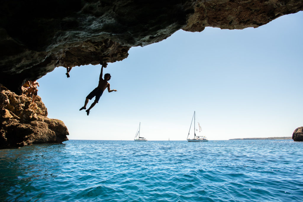 Un homme grimpe juste au dessus de la mer sur une paroi rocheuse à Majorque, destination sportive pour un séjour d'escalade
